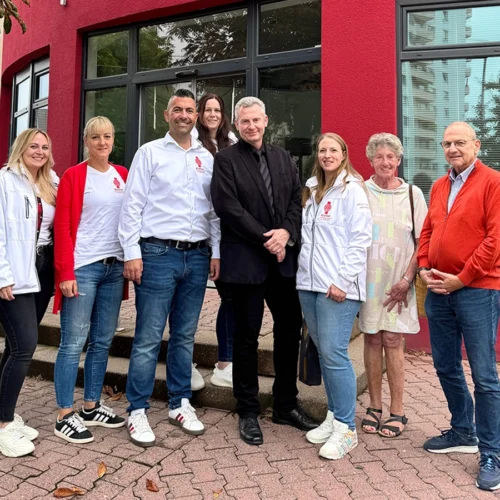 Acht Personen stehen nebeneinander in einer Reihe draußen vor dem Gebäude und lächeln in die Kamera.