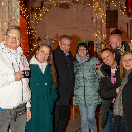 Mehrere Personen auf dem Weihnachtsmarkt nebeneinander stehend lächeln in die Kamera